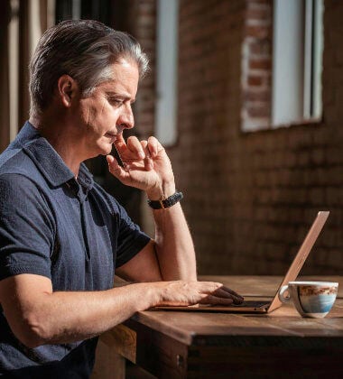 An older man uses a laptop whilst sitting at a desk